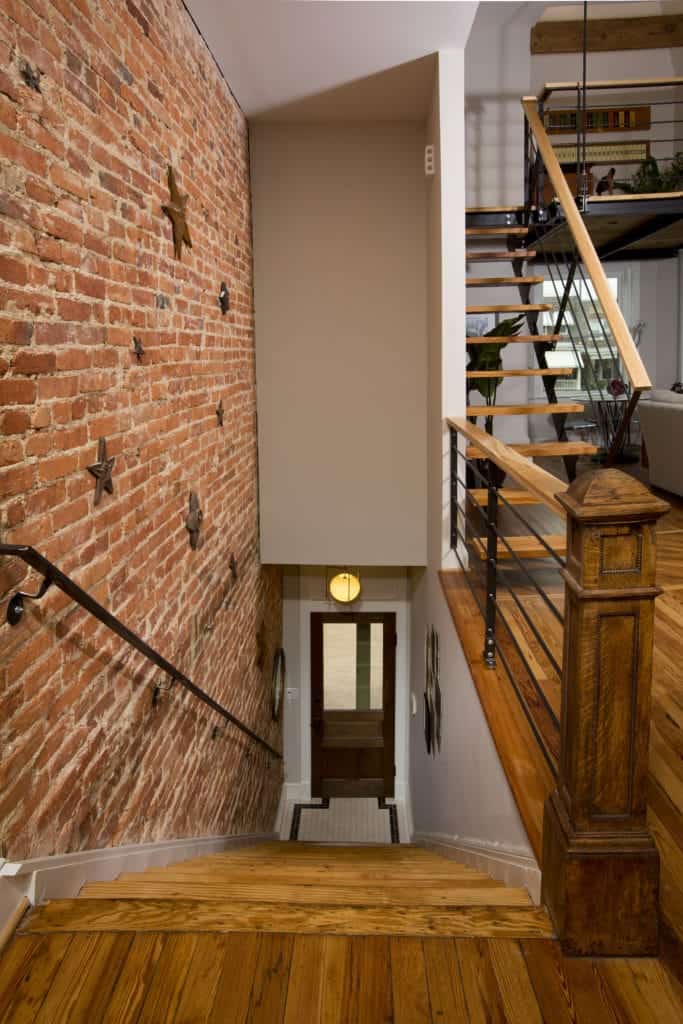 这个工业风格的门厅有一个木质的正门，上面有一个工业风格的壁灯。小门厅直接通向木楼梯，楼梯一侧有红砖墙，另一侧有白墙，通往房子的其他部分。