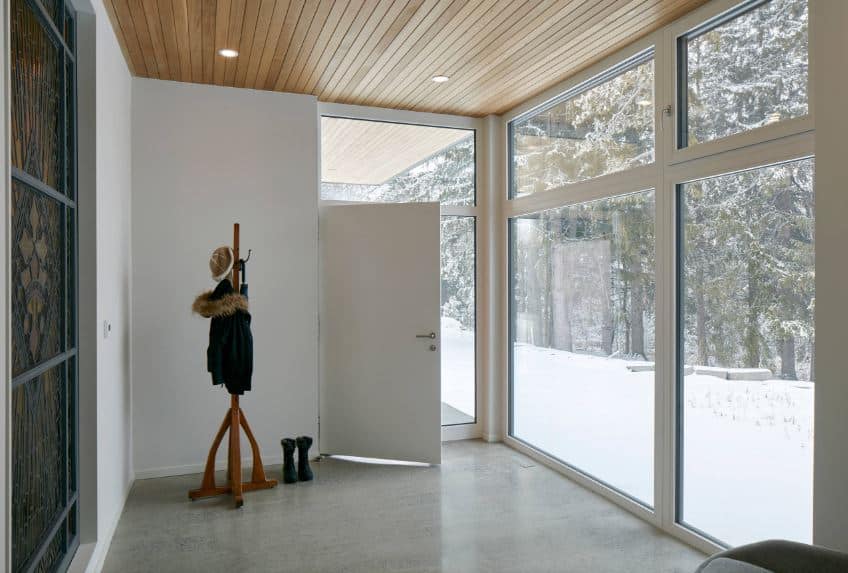 这个工业风格的门厅有玻璃墙，以展示外面充满雪和树木的风景之美。简单的工业风格的地板装饰着一个站立的木制架子，用来放夹克和帽子，与木制天花板很好地搭配。