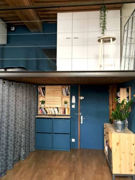 这个门厅有一个低矮的木质天花板，也作为阁楼的地板，上面有金属丝栏杆。这与蓝色的主门很好地融合了墙壁，旁边的橱柜与深色的硬木地板相得益彰。