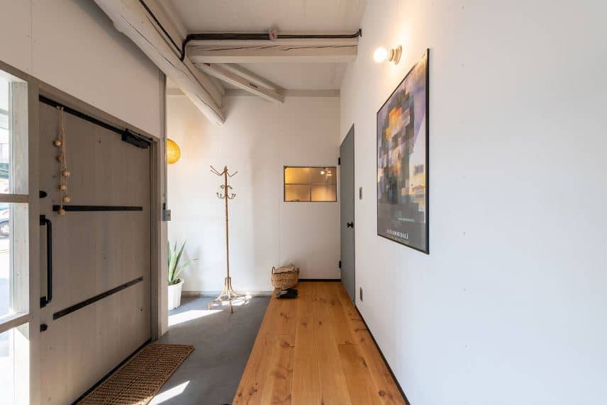 这个迷人的门厅有一个带侧灯的大木门。灰色的混凝土地板与门对面白色墙壁上的硬木地板相呼应，白色墙壁上装饰着彩色的海报，用灯泡照亮。