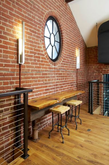这座工业风格门厅的红砖墙上有一张嵌壁式桌子，桌腿是水管。它还搭配了一对木制凳子，凳子腿上还有管子。这是一个很好的背景圆形窗户两侧的现代壁灯。