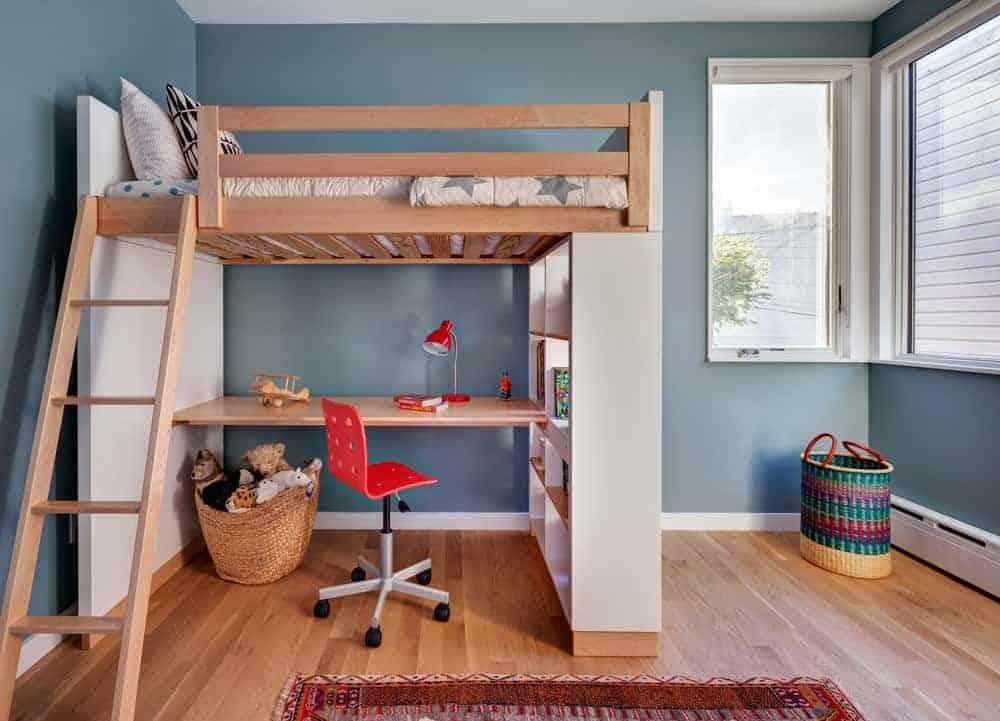 这间卧室有一张阁楼床，一张桌子放在蓝色的墙上。它包括一个红色转椅和棕色地毯，铺在宽阔的木板地板上。