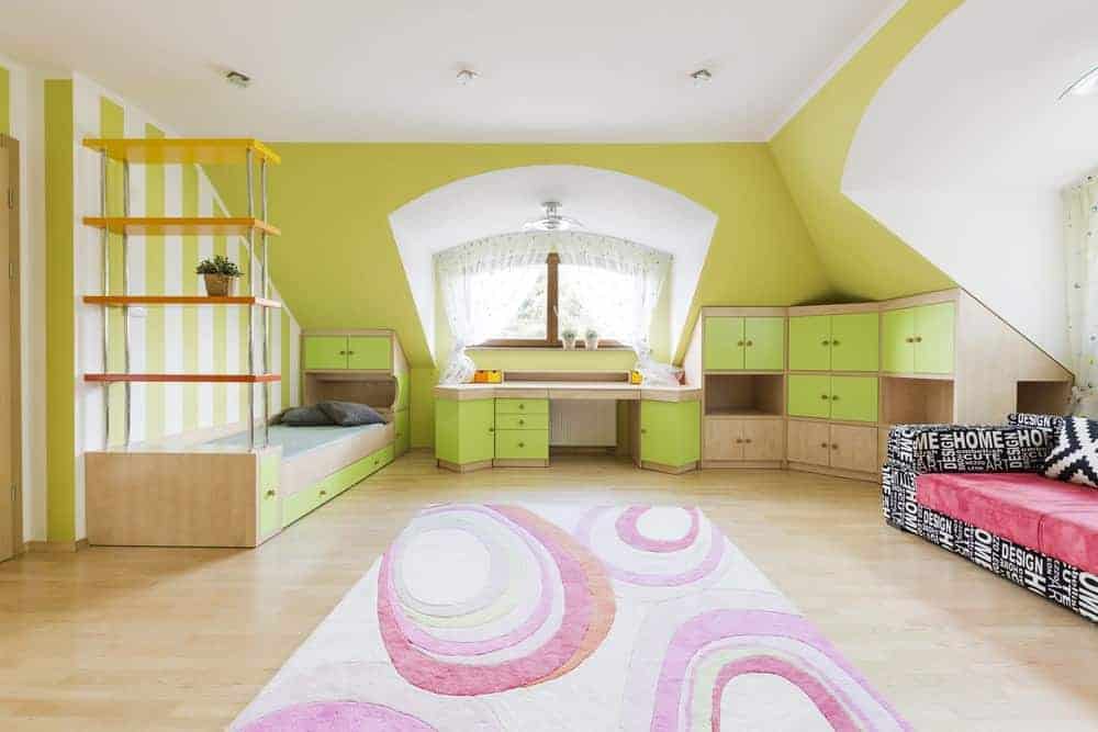 在这间绿色的卧室里，黑色的沙发和粉红色的组合靠垫格外显眼，卧室里摆满了内置家具，浅色硬木地板上铺着迷人的区域地毯。