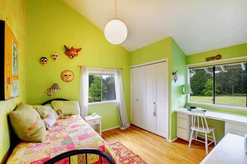 绿色的卧室设计与头墙装饰和一个磨砂玻璃全球吊坠悬挂在拱形天花板。它有一张黑色的金属床，与内置衣柜和白色办公桌形成鲜明对比。