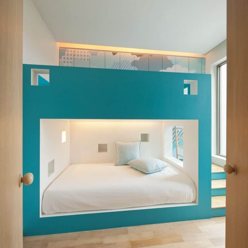 一扇轻木双开门通往这间时尚的卧室，配有一个大的嵌入式双层床，蓝绿色的口音几乎占据了房间的整个空间。