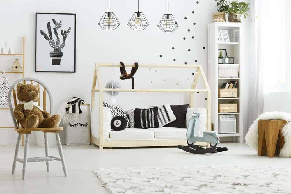 在这间儿童卧室里，一只可爱的泰迪熊坐在木制的圆形靠背椅上，它有一个天篷小屋海报床和一个覆盖着白色人造毛皮毯子的时尚座椅。
