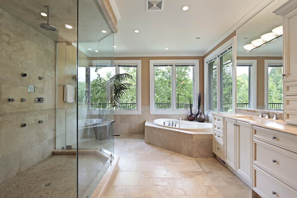 这间主浴室给人一种特别而宁静的感觉。我喜欢它的简洁，温暖和干净的配色，巨大的角落窗户，让你看到外面的绿色植物，以及淋浴房和浴缸的奢侈尺寸。漂亮的米色石材瓷砖被用于整个地板，浴缸的壁板，甚至是浴缸周围的小后挡板。我认为在浴室的角落里有一个按摩浴缸是一种很好的感觉，尤其是它位于那么大的窗户下面。这个超级简单的虚荣心告诉我们，这个房间更多的是用来放松，而不是用来为你的一天做准备。非常宽敞的淋浴房配有瀑布水龙头和地面上的土耳其风格瓷砖。我真的很喜欢这个浴室的外观!