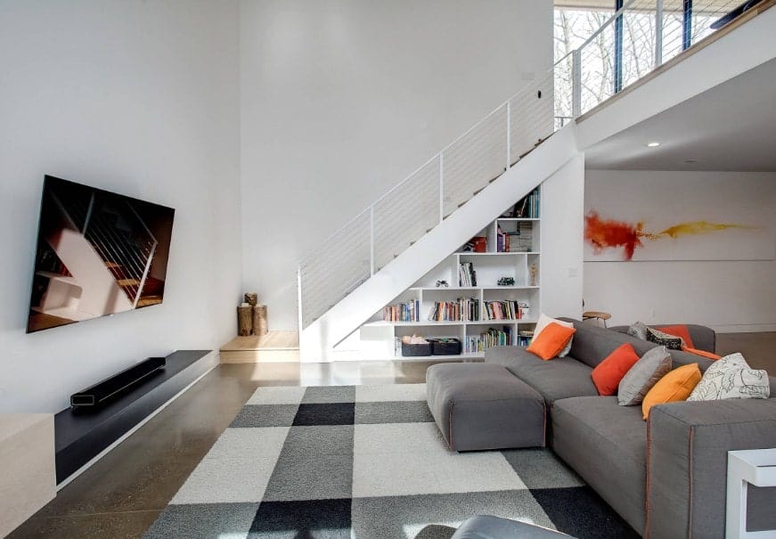 这间客厅提供一个舒适的灰色沙发，在时尚的区域地毯上设有一个脚凳。前面有一个大宽屏电视。