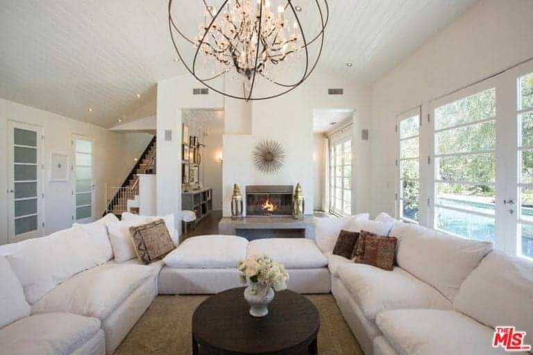白色客厅配有白色沙发，由白色软垫连接，并由华丽的吊灯照明。