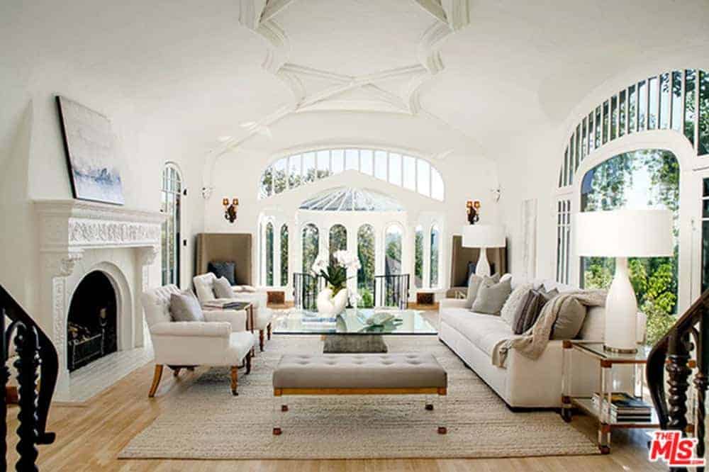 这所房子拥有一间客厅，配有一组白色座椅和一个玻璃顶部的中央桌子，以及装饰精美的天花板下的壁炉。