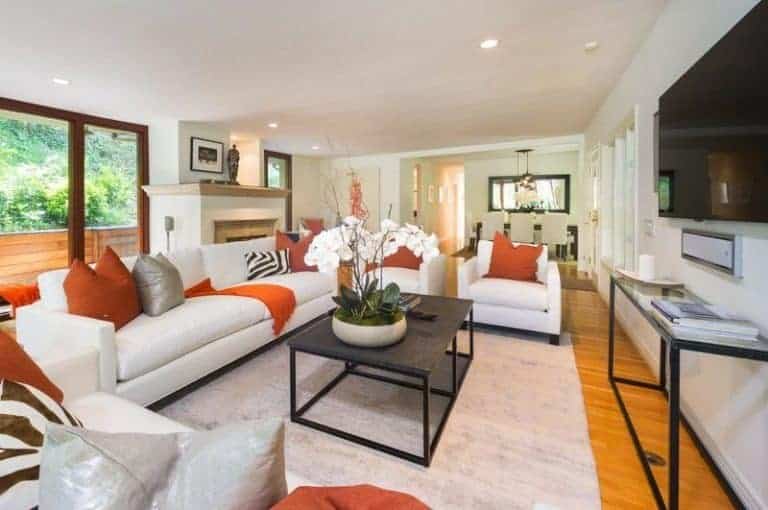 这间客厅设有一套带有橙色基调的白色座椅，以及墙上的大型宽屏电视。