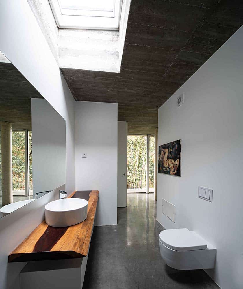 这是浴室的景观，它有一个长而窄的设计，通过卫生间对面的木制浮动梳妆台上方的大天窗来照亮。