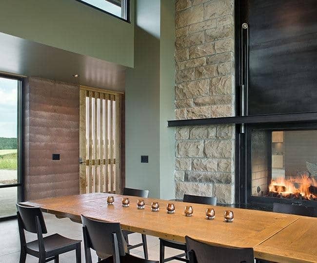 长矩形木餐桌搭配黑色木制椅子借给壁炉的框架是固定的,米色的大支柱石头,旁边墙上的亮绿色色调突出但匹配的米色地板瓷砖。