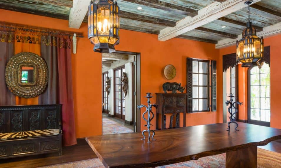 这间餐厅的木质和朴实的部落装饰与橙色的墙壁相映成趣。这些装饰也与质朴的木制餐桌和硬木地板相匹配，硬木地板主要由彩色地毯覆盖。
