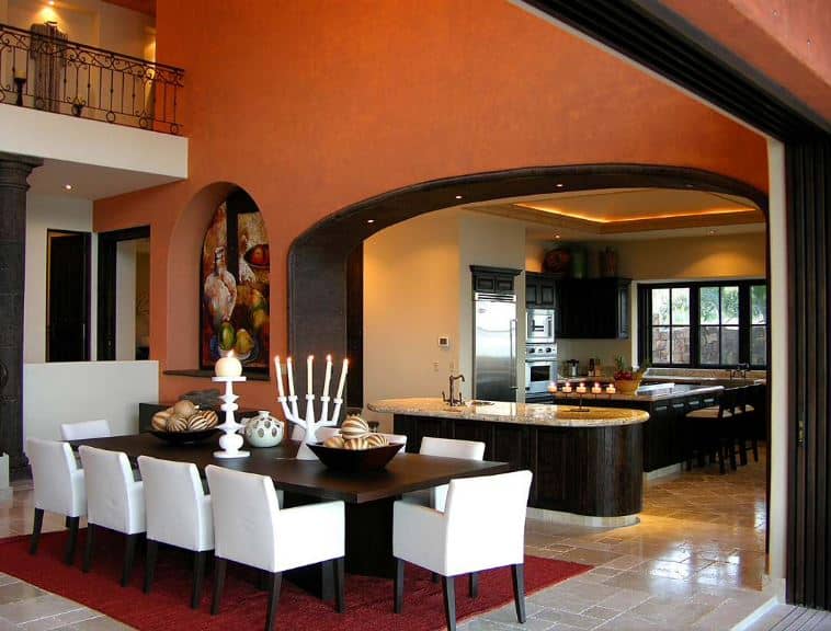 厨房和用餐区由一条深棕色的拱形入口分开，与木制餐桌相呼应。这与白色的椅子垫和顶部的装饰形成对比。土黄色的墙壁缓和了这种对比。