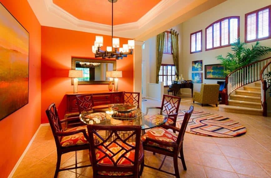 这间迷人而温暖的餐厅位于门厅的一角。它有橙色的墙壁和天花板，由吊灯的黄色灯光增强，与镜子两侧的台灯相匹配，俯视着玻璃桌面。