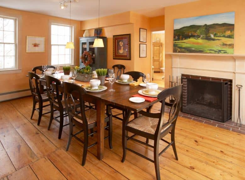 这幅彩色的草甸画与阳光色的橙色墙壁完美契合，与深色木质餐桌和深色木椅形成鲜明对比，与壁炉旁的硬木地板相映成趣。