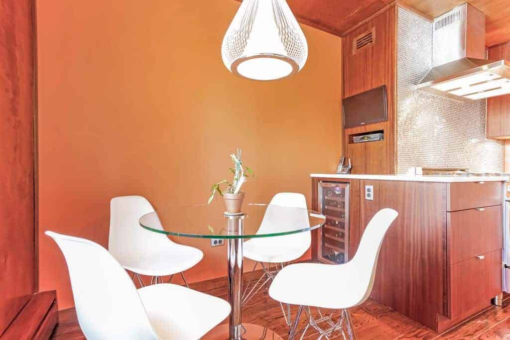 白色的现代椅子与圆形玻璃桌完美搭配，不锈钢支架与椅子腿相配。这些现代元素在墙壁和木结构的泥土背景下脱颖而出。