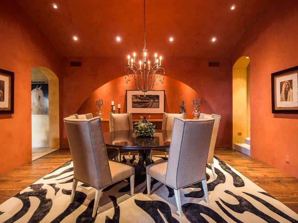 斑马纹地毯覆盖了大部分硬木地板，在橙色的墙壁和天花板上很显眼，天花板上有黄色的凹形灯，一盏枝形吊灯使黑色木制餐桌和软垫椅子变得温暖起来。