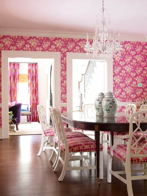 迷人的餐厅覆盖着粉红色的碎花壁纸，与白色软垫椅子周围的木制椭圆形桌子，上面有一对罐子。