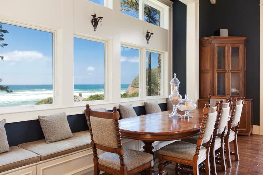 一个宁静的餐厅拥有一个木制的餐厅，融合在木木板地板，以及一个内置的长凳下面的玻璃镶板窗户俯瞰一个令人惊叹的海滩景色。