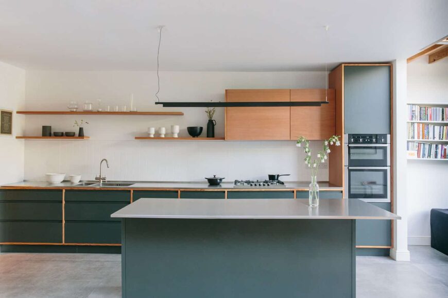 现代定制厨房，深绿色橱柜门在道格拉斯冷杉框架，道格拉斯冷杉浮动货架和墙壁单元，不锈钢台面，混凝土瓷砖。
