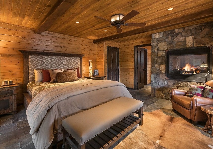 带木墙和天花板的大型主卧室。屋内有一座巨大的石砌壁炉和一套优雅的床具。