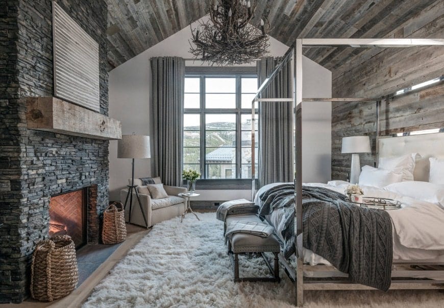 灰色质朴的主卧室设有一个大舒适的床和一个大的石头壁炉，由一个惊人的吊灯挂在拱形天花板上。