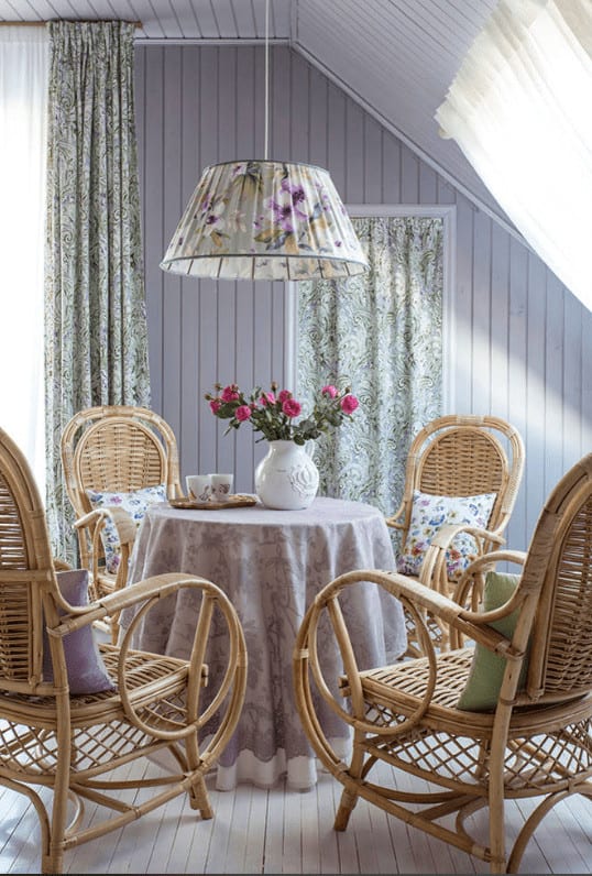 一个可爱的圆顶吊灯悬挂在圆形餐桌上，餐桌上覆盖着淡紫色的布，周围是藤椅，藤椅上有迷人的枕头。