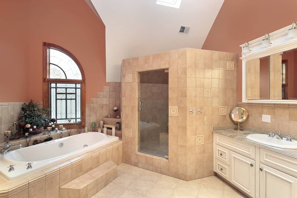 宽敞的主浴室，红墙和瓷砖地板。步入式淋浴间也是用瓷砖砌成的。窗户附近也有个浴缸。