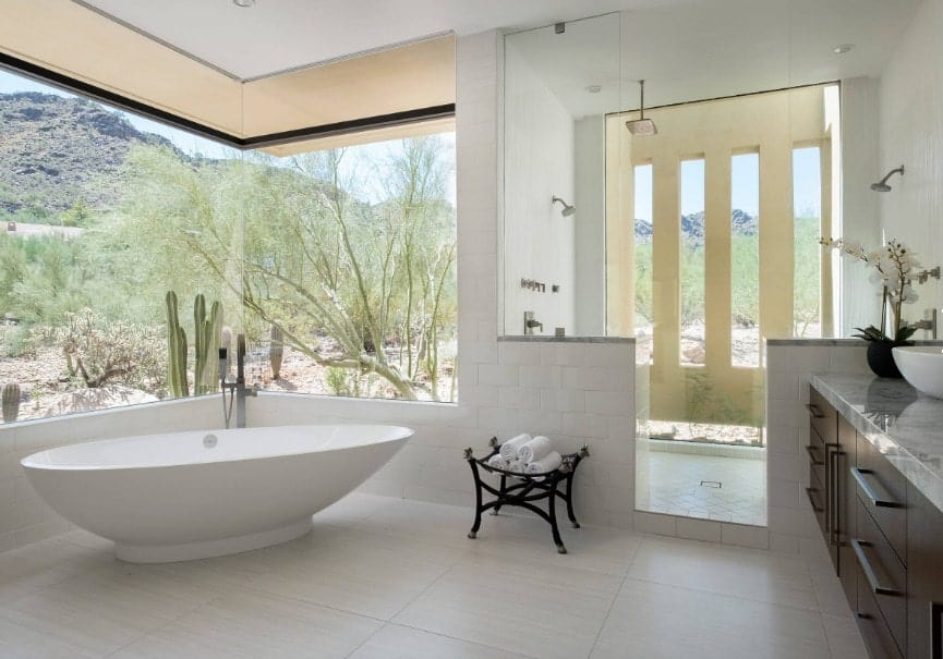 这间主浴室设有白色瓷砖地板和玻璃窗，可俯瞰令人惊叹的室外景色。有一个独立的浴缸和一个开放式的淋浴间。