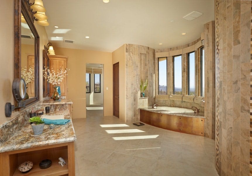 大型主浴室，靠近窗户的深浸浴缸和优雅的水槽柜台，被华丽的壁灯忽视。