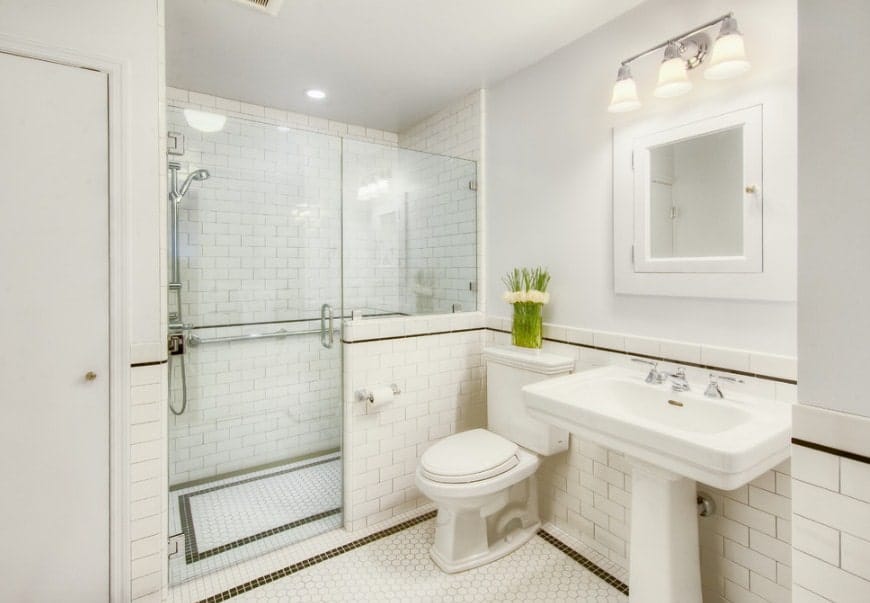 明亮的主浴室，白色瓷砖地板和墙壁。房间提供了一个步入式淋浴和一个底座水槽由华丽的壁灯照明。