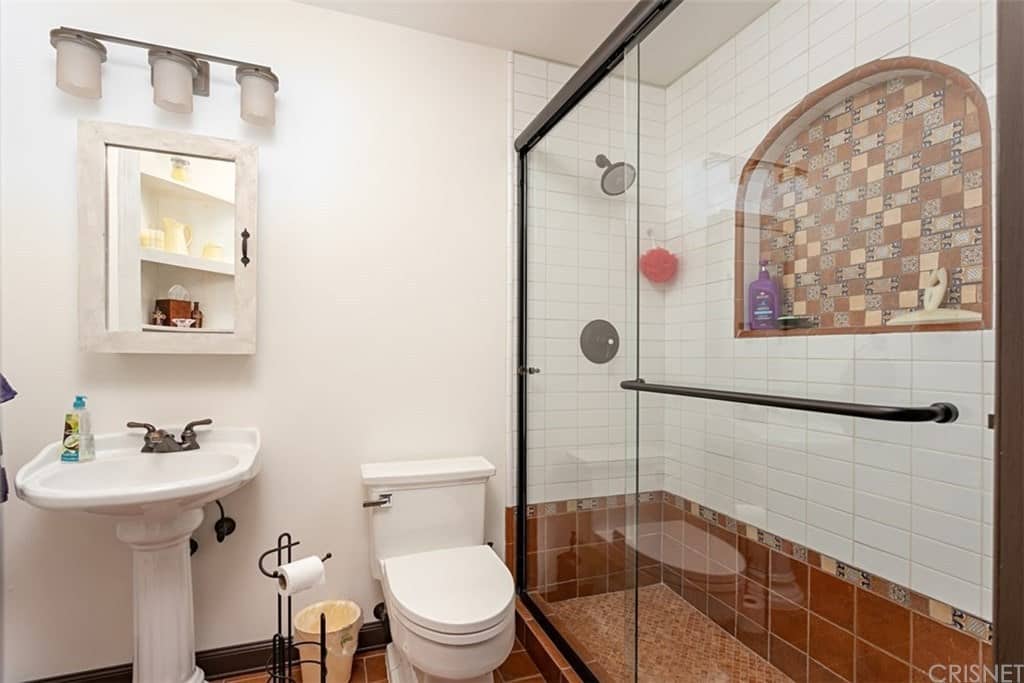 这个简单而温馨的西南风格浴室的亮点是迷人而朴实的巧克力棕色地板瓷砖，使白色马桶和底座水槽脱颖而出。这些土质瓷砖延伸到淋浴区较低的墙壁，以及其上部墙壁上的小凹室。