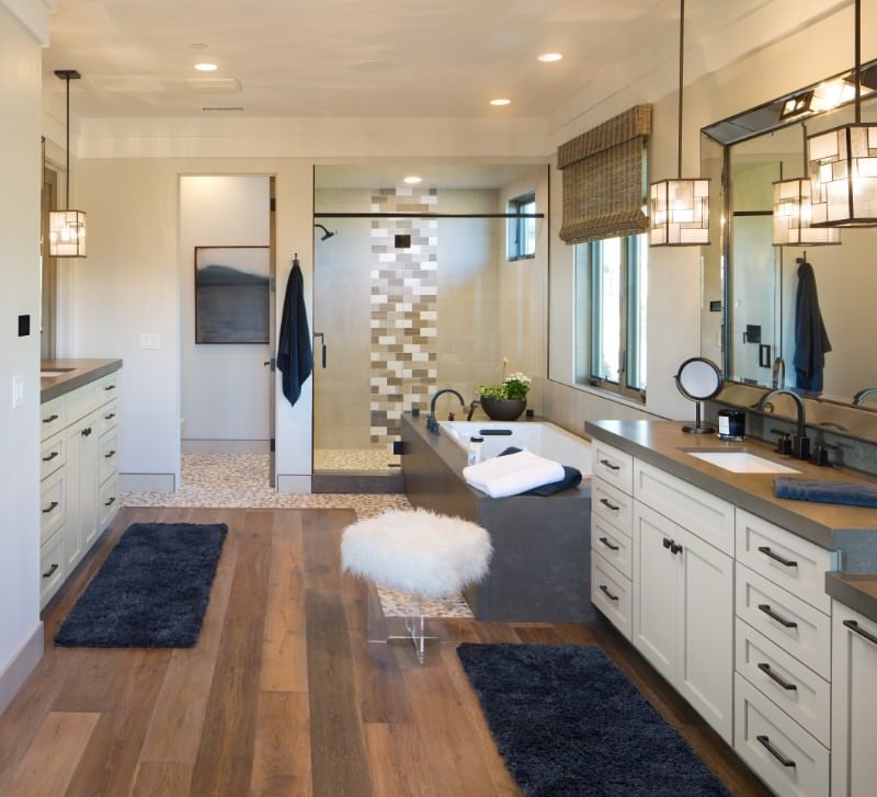 这间西南风格的主浴室有足够的空间放置两个独立的梳妆台，上面有相同的白色橱柜和抽屉，上面有灰色的台面。一个在灰色浴缸旁边，另一个在它对面靠门的墙上。