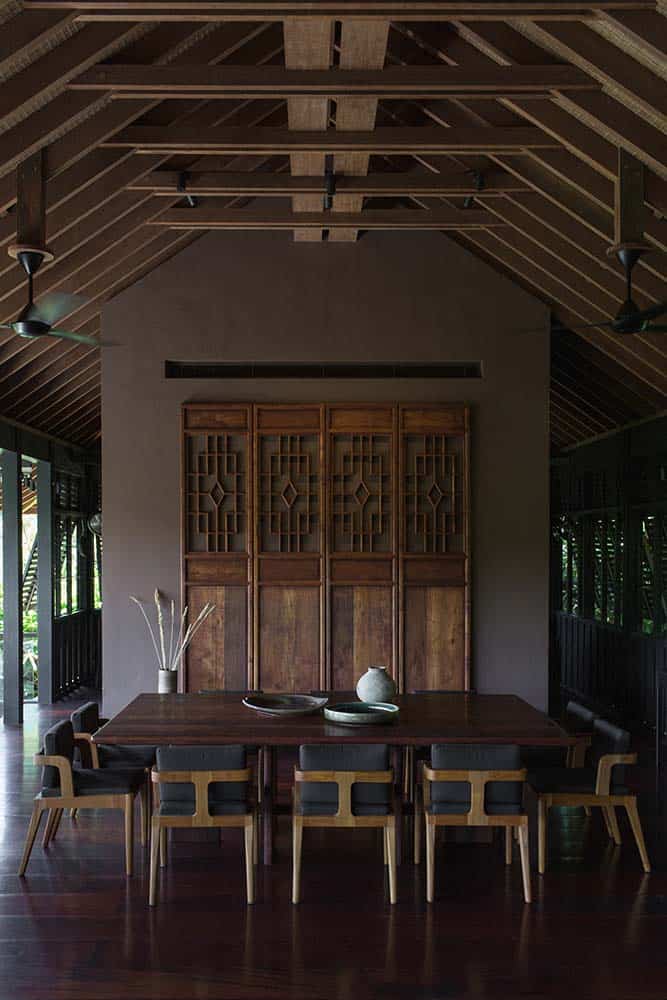这是这所房子的餐厅，有一张长方形的木制餐桌，周围是软垫椅子，顶部是木制拱形横梁天花板，远处的墙上装饰着木板，上面有复杂的雕刻。