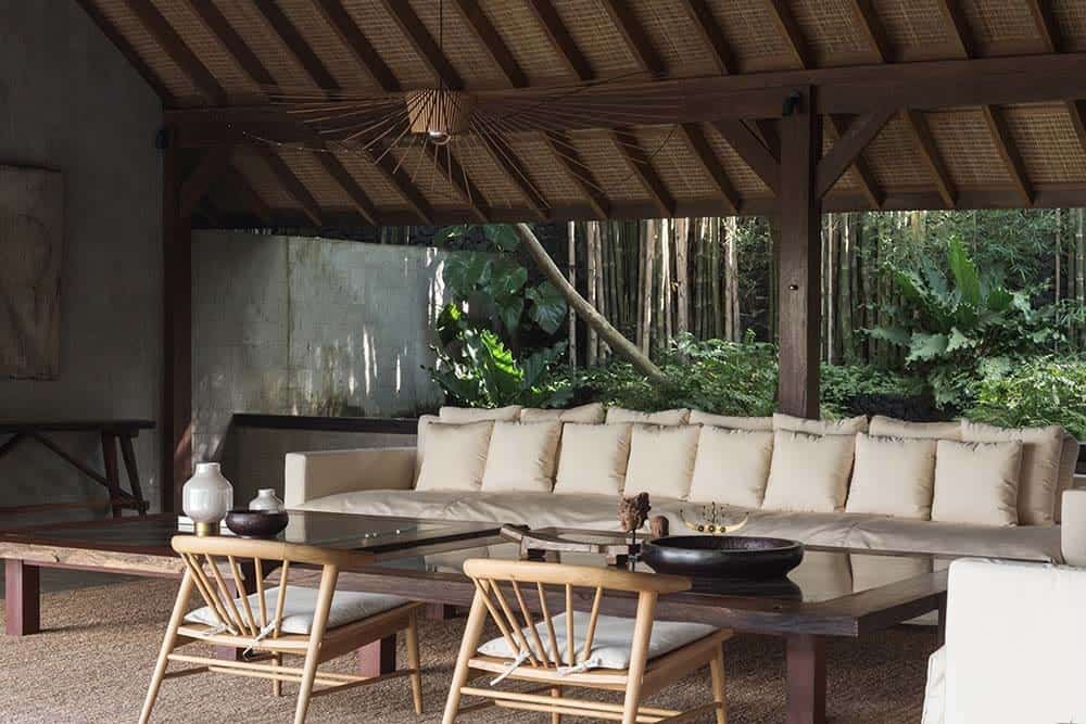 这是一间有拱形木制天花板的客厅，大玻璃咖啡桌上方挂着一盏装饰性的灯，与之搭配的米色沙发被自然光照亮。