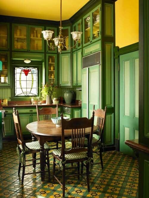绿色的餐厅里有格子软垫椅和圆形餐桌，黄色的天花板上挂着一盏复古的枝形吊灯。