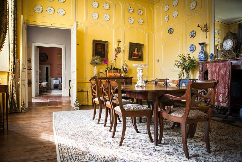 高雅的黄色木质墙面上装饰着各种经典画作和装饰性餐具。这为木制餐桌和椅子在大图案区域地毯上设置了更高的优雅水平。