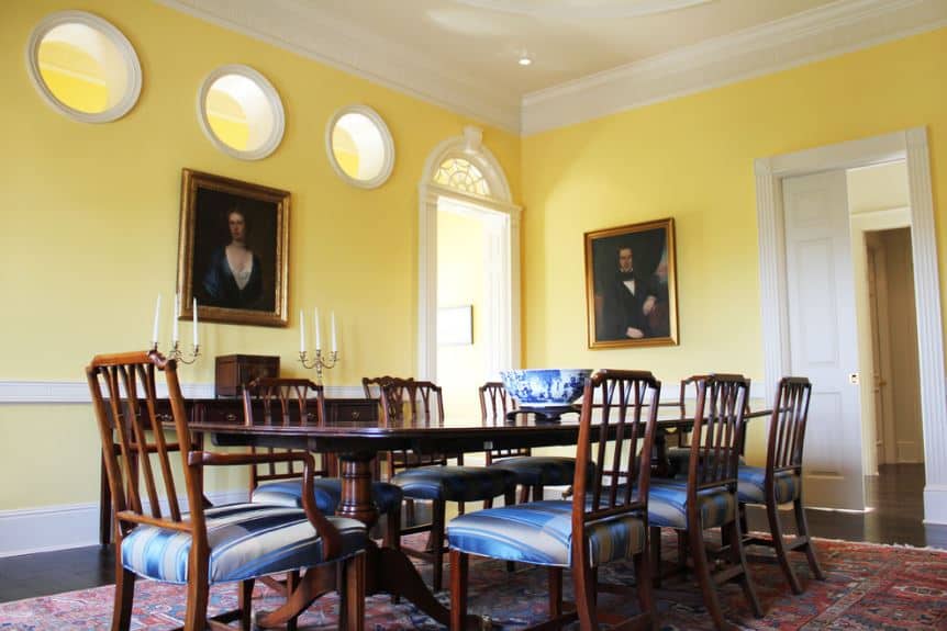 餐厅简单的黄色墙壁被挂在墙上的几幅经典画作抬高了，墙壁上有靠近白色天花板的圆形窗户。这是一个很好的背景大木制餐桌和它的木椅，有蓝色条纹的坐垫。