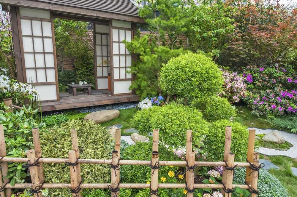 这个亚洲风格的小花园用竹条围起来，与旁边的小竹喷泉相匹配。这个禅意花园由各种开花灌木和不同的树木组成，为小木屋设置了一个美妙的框架。