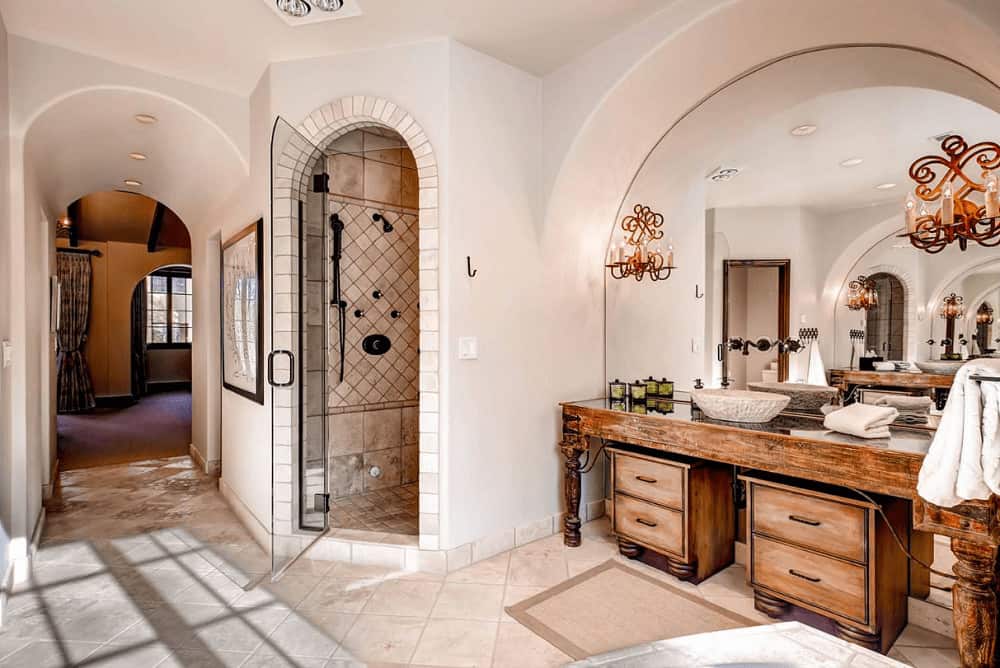 这间主浴室设有步入式淋浴间和天然木容器水槽梳妆台，配有一面装有漂亮蜡烛烛台的拱形镜子。