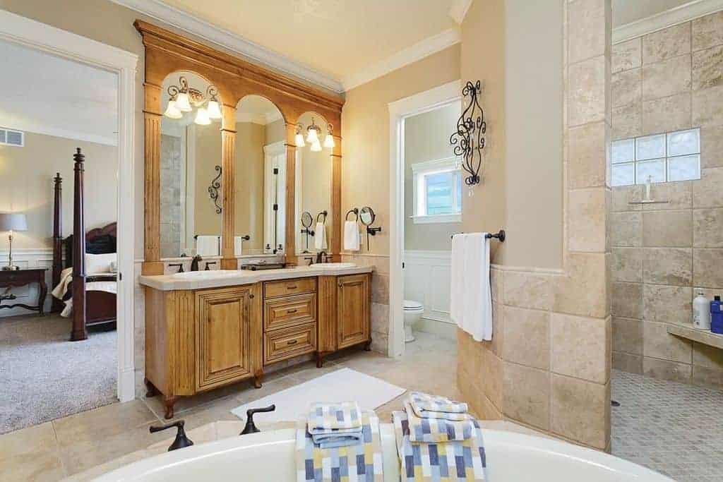 明亮的主浴室配有淋浴和厕所区，以及一个深浸浴缸，面向木制洗手台，配有锻铁固定装置。