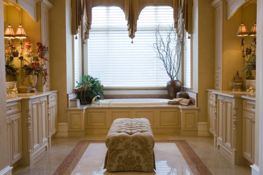 这间主浴室面向梳妆台，中间有簇绒软脚凳，上方是大理石地板。它包括玻璃窗边的一个浴缸，上面装饰着迷人的帷幔。