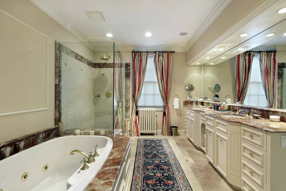红色条纹窗帘和可爱的碎花裙架在这个米黄色的主浴室里很显眼，浴室里有一个落地式浴缸和双水槽梳妆台，上面有优雅的大理石柜台。