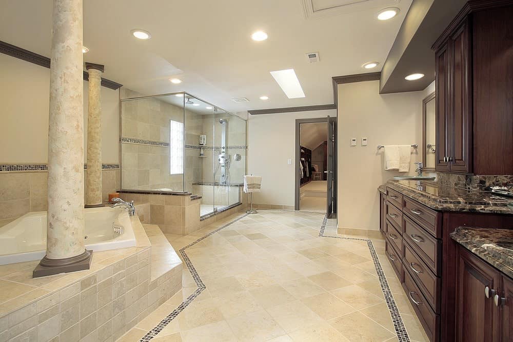 米色的主浴室设有步入式淋浴间和配有一对柱子的浴缸。它包括一个大的深色木材梳妆台，上面有黑色花岗岩柜台。