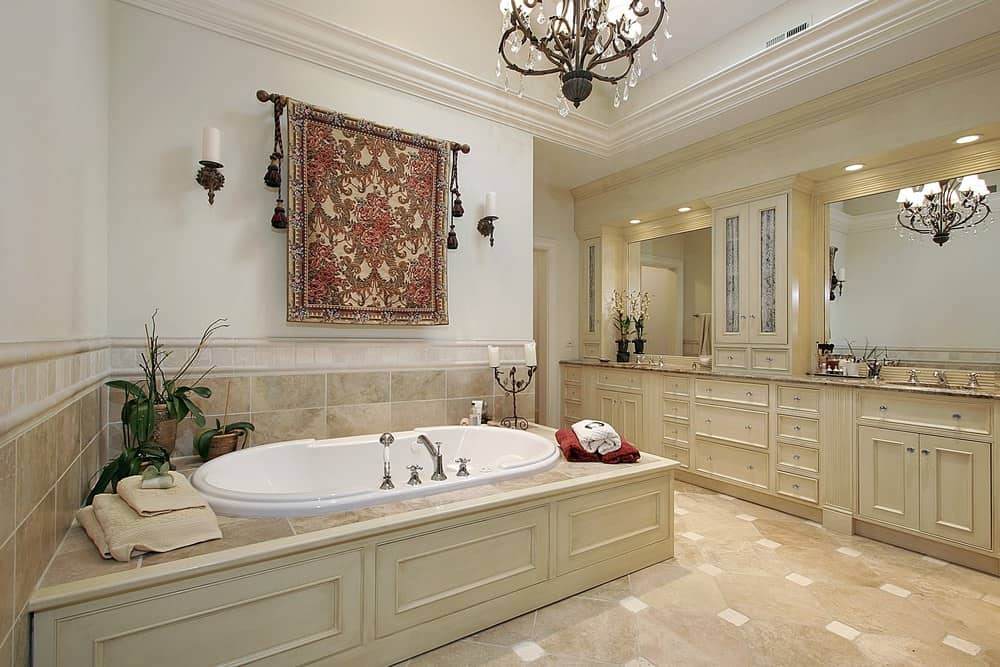 优雅的主浴室装饰着一盏花哨的吊灯和一幅华丽的挂毯，挂在深泡浴缸上方，上面有新鲜的盆栽植物。