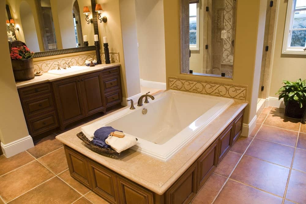 温暖的主浴室提供了一个单独的洗手台，由一个华丽的壁灯和一个覆盖着深色木护壁板的浴缸照亮。