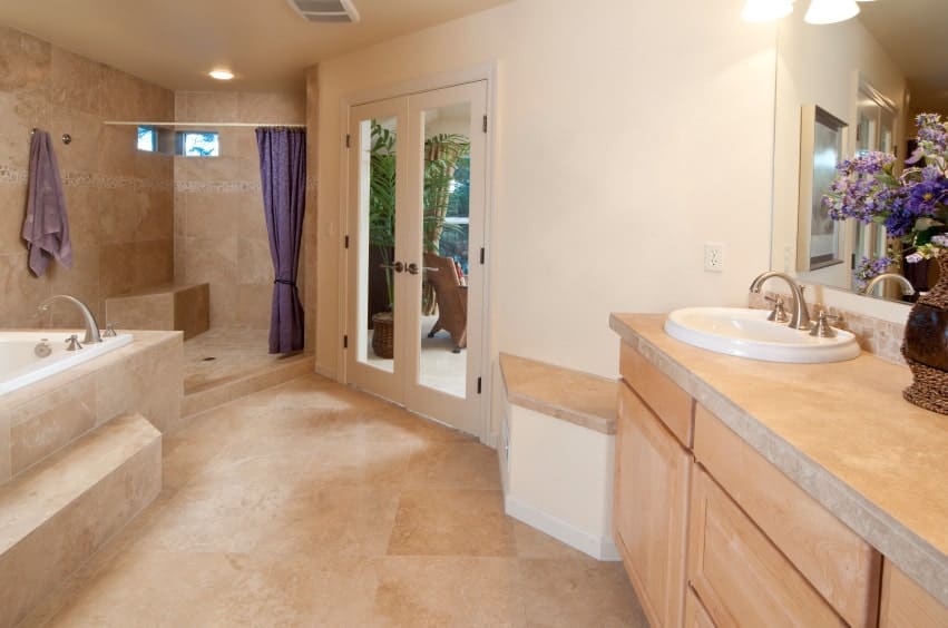 地中海主浴室，深浸泡浴缸和淋浴区封闭在紫色窗帘。它包括一个浅色的木制洗手台，侧面有一个内置座椅。