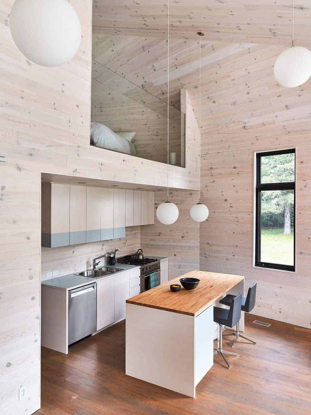 这间小厨房有一扇玻璃窗，高高的木板天花板上装有球形吊灯，厨房里有一个带黑色皮凳子的早餐座，正对着轻木橱柜。
